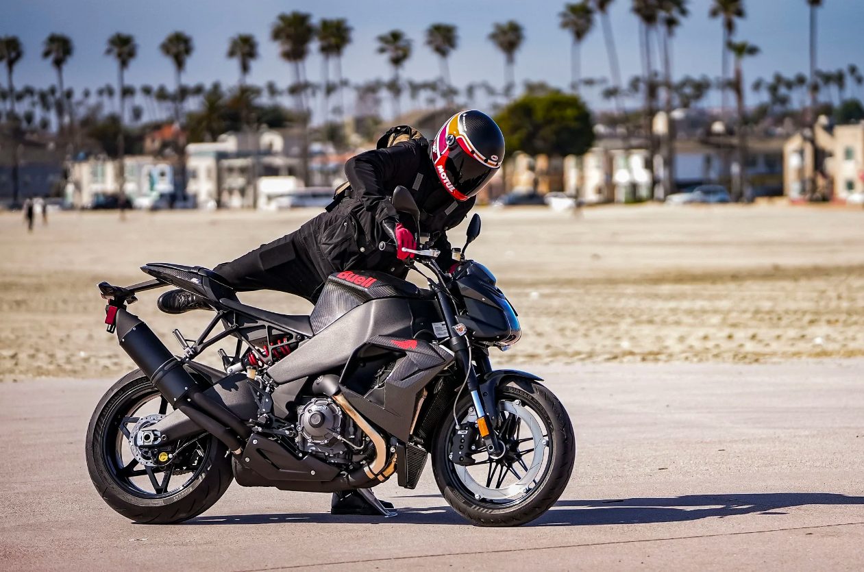Buell 1190SX streetfighter with rider leaning over the tank on a beachfront lot