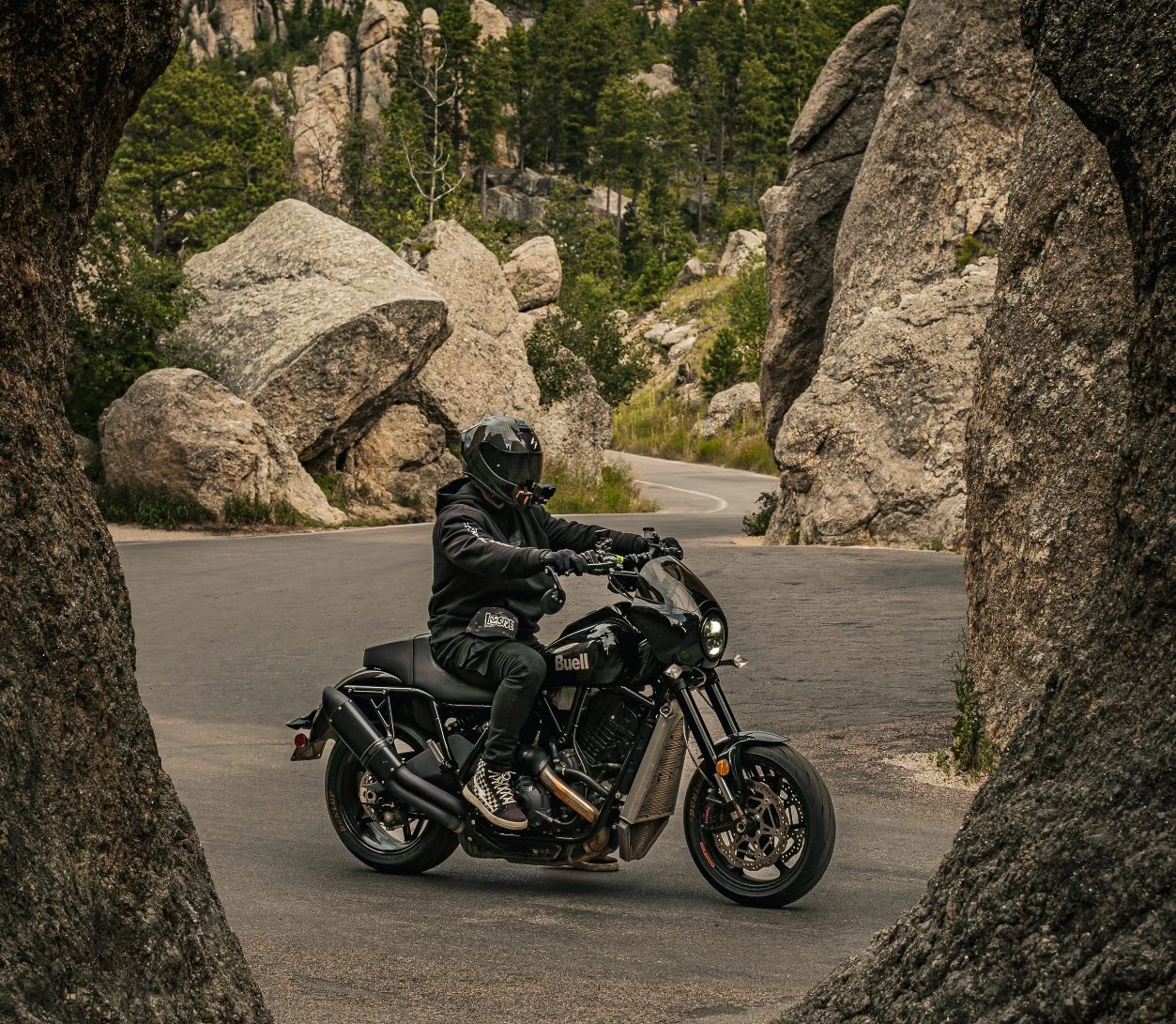 Rider on a black Buell Super Cruiser on a winding road between granite boulders